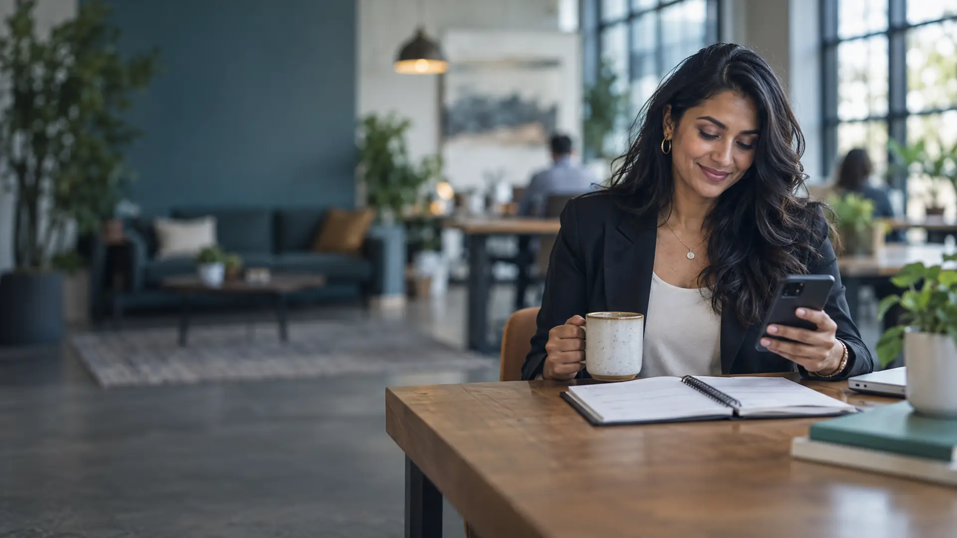 Business coach in a co-working space smiling at her phone, a coffee and an open planner on the table